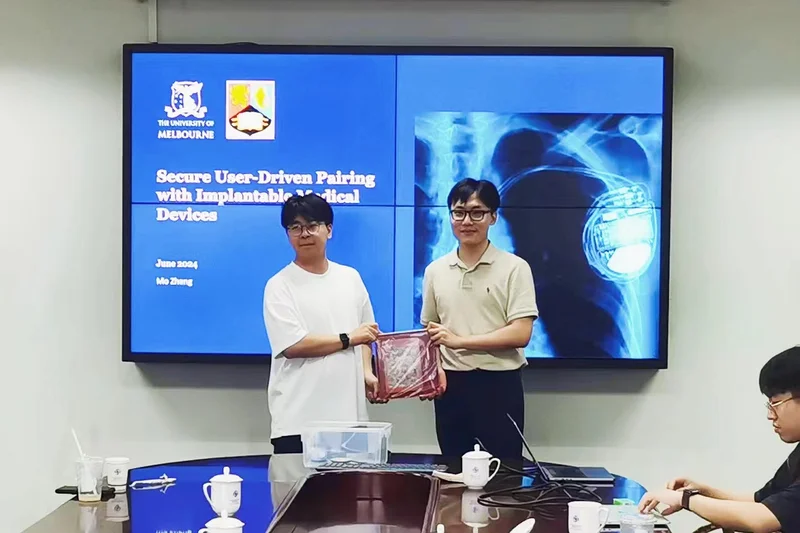 Shaking hands in a meeting room, with a talk's title slide and a pacemaker X-ray on the screens behind